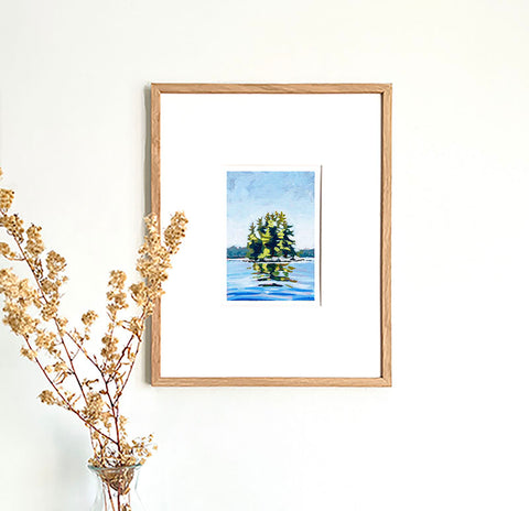 lake wall art print of trees on an island surrounded by shimmering blue water in a wood frame